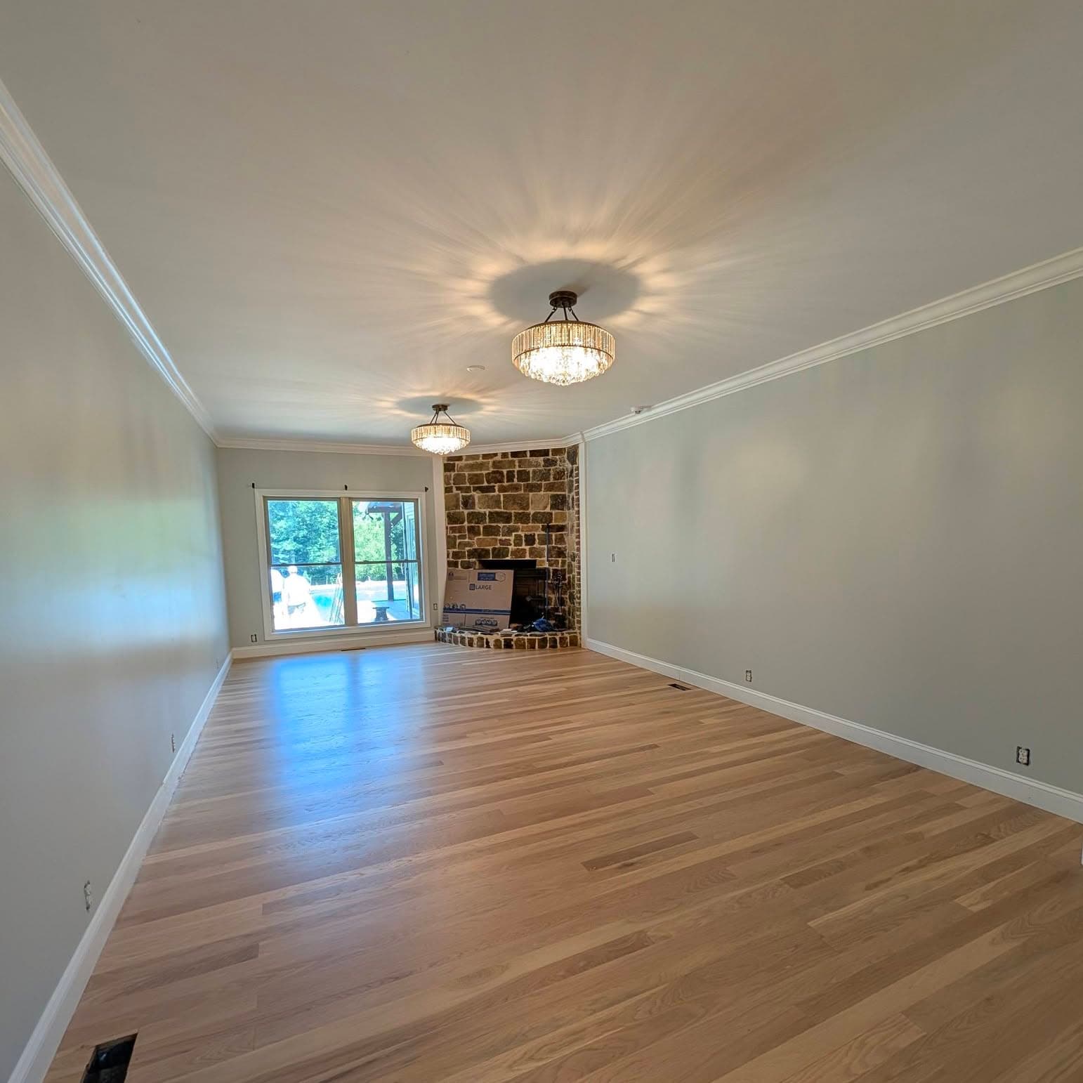 Natural oak hardwood floor in a long living room with a stacked-stone corner fireplace, a job by Alabama Hardwood Restoration