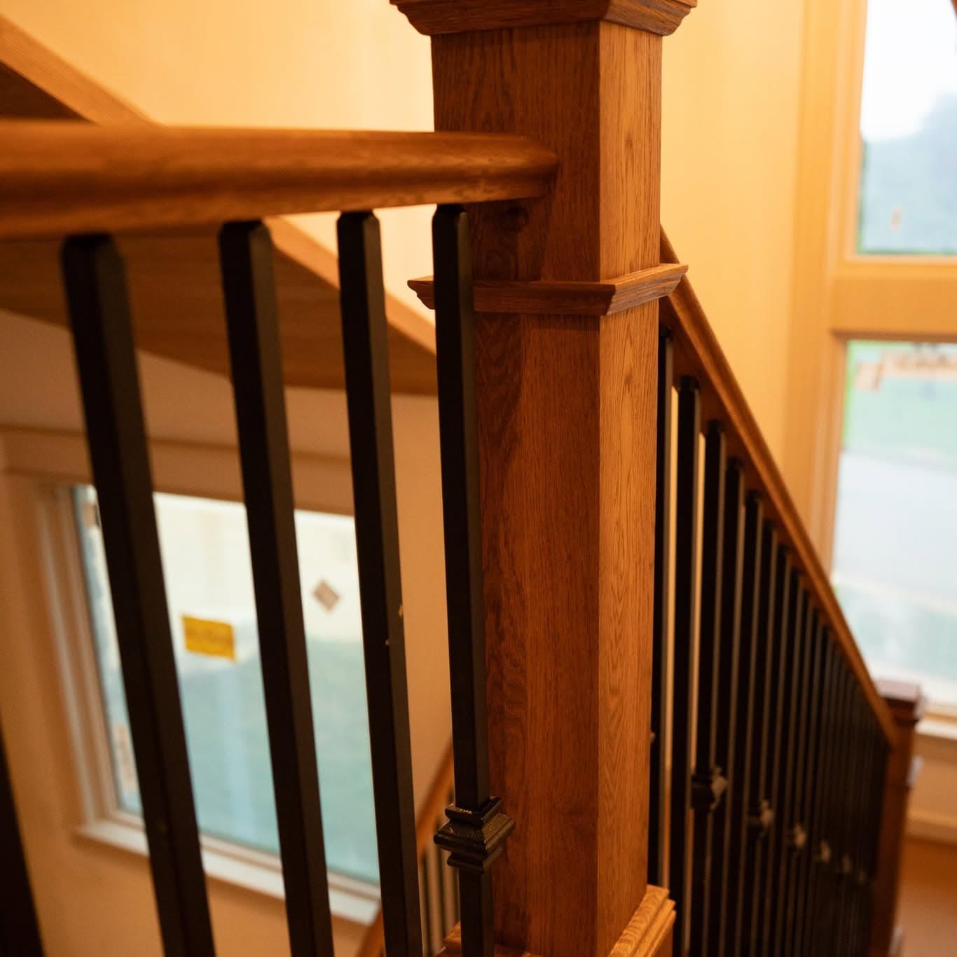 Close-up of a stained square wood newel and matching handrail with black metal balusters, a job by Alabama Hardwood Restoration